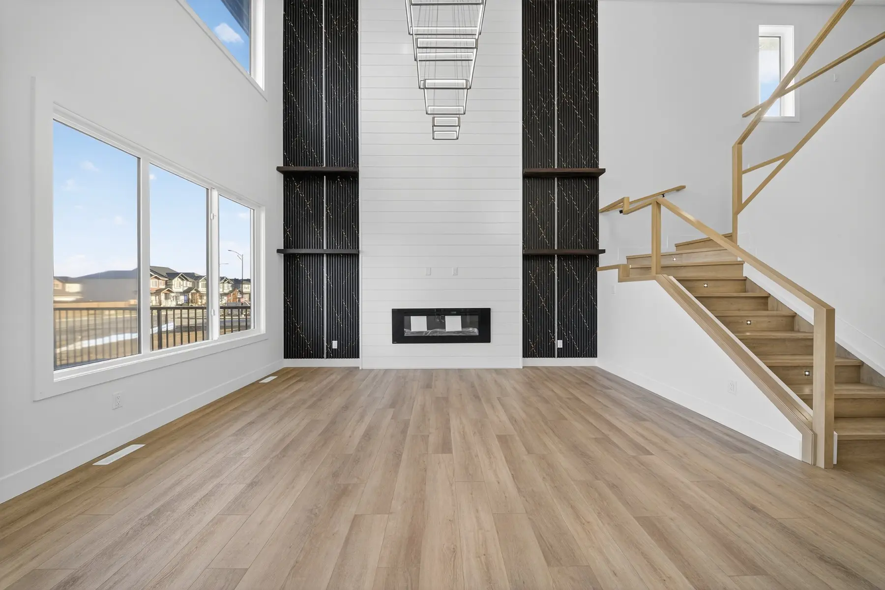Open-to-above living room with a tall black feature wall and wood staircase in the Cavanagh residence